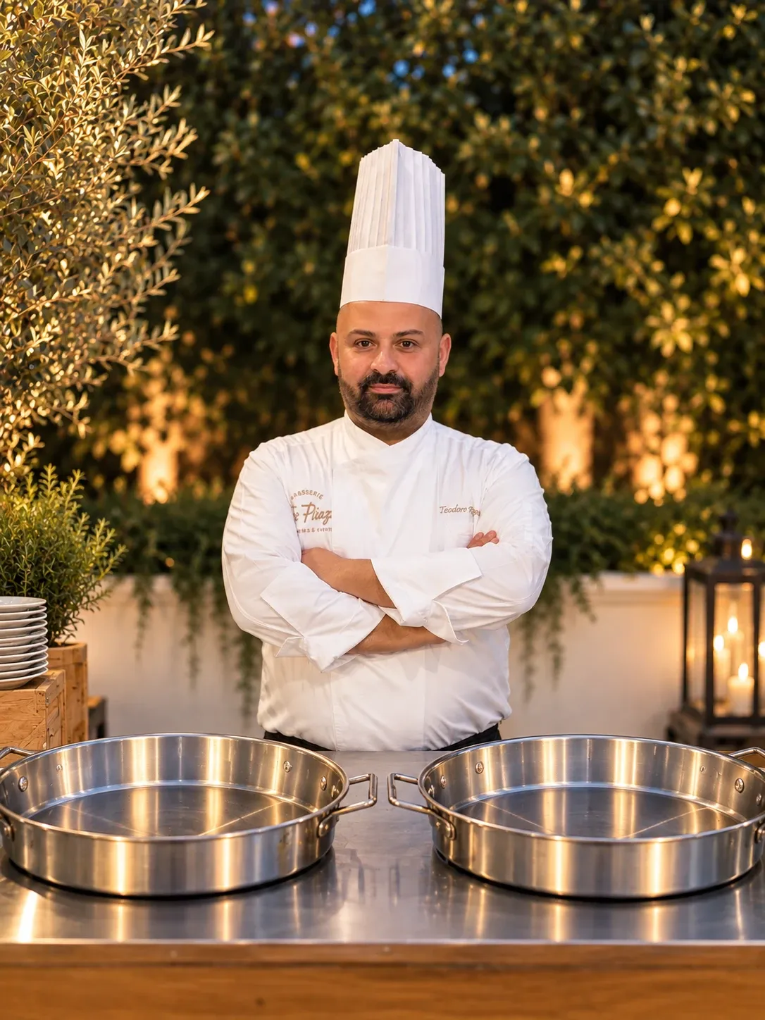 Lo chef in divisa, a braccia conserte dietro le padelle, pronto per il servizio in giardino